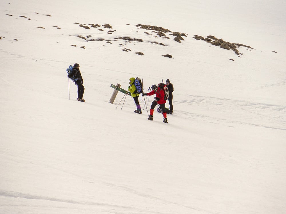 esquiadores subiendo una montaña nevada